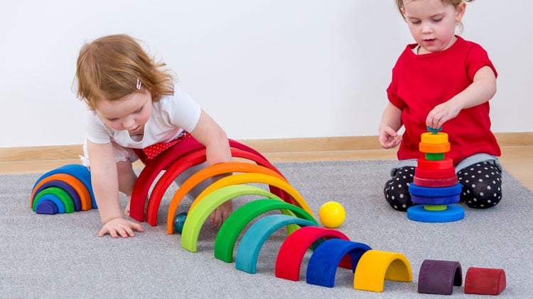 Kinder spielen mit einem Holzregenbogen - der auch in Waldorfkindergärten seine Anwendung findet.