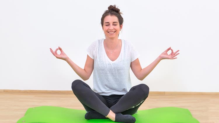 Frau sitzt entspannt auf einer Yoga-Matte von Betzold.