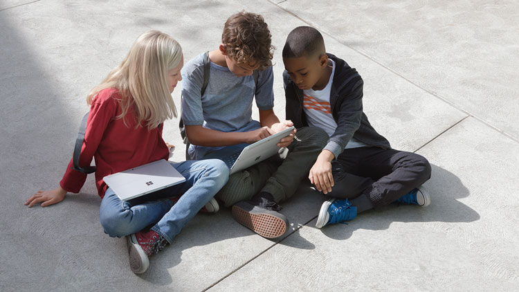 Schüler sitzen draußen und arbeiten mit Microsoft Surface.