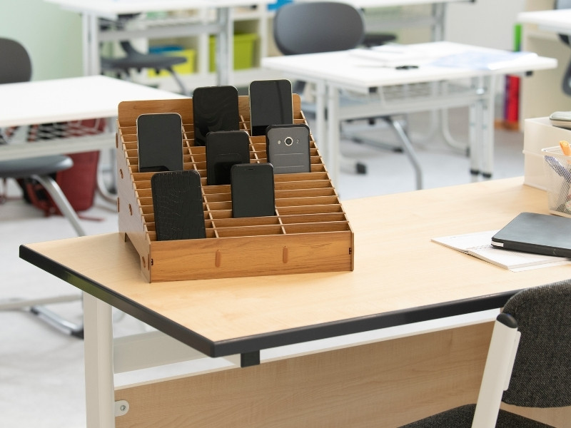 Handygarage aus Holz mit Fächern für Smartphones auf einem Lehrerpult