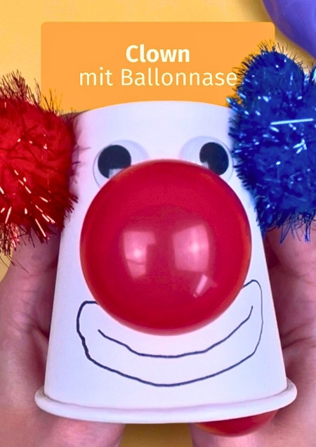 Clown gebastelt aus einem Pappbecher, dem eine Nase aus einem roten Luftballon wächst.