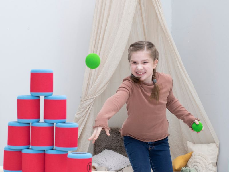 Mädchen wirft mit Ball auf gestapelte Dosen