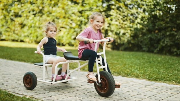 Zwei Kindergartenmädchen auf Kinderfahrzeug im Garten