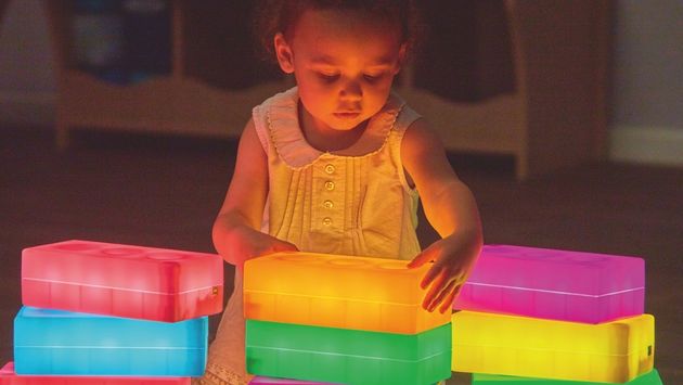 Kleines Kind stapelt bunt leuchtende Bausteine in abgedunkeltem Raum