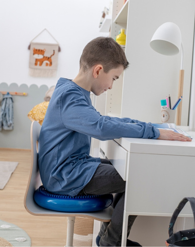 Junge sitzt mit Sitzkissen auf einem Stuhl am Schreibtisch
