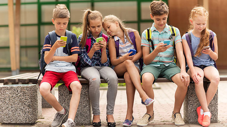 Schüler sitzen mit Handys auf Bank