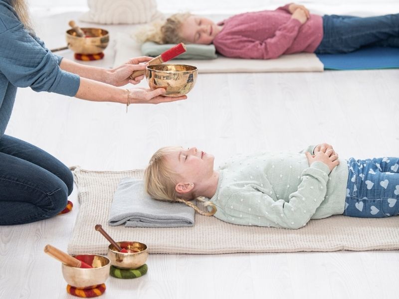 Zwei Kinder liegen auf dem Boden und lauschen den Tönen einer Klangschale
