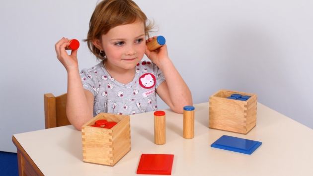 Mädchen schüttelt die gefüllten Zylinder der Soundbox umd das Geräusch zu bestimmen