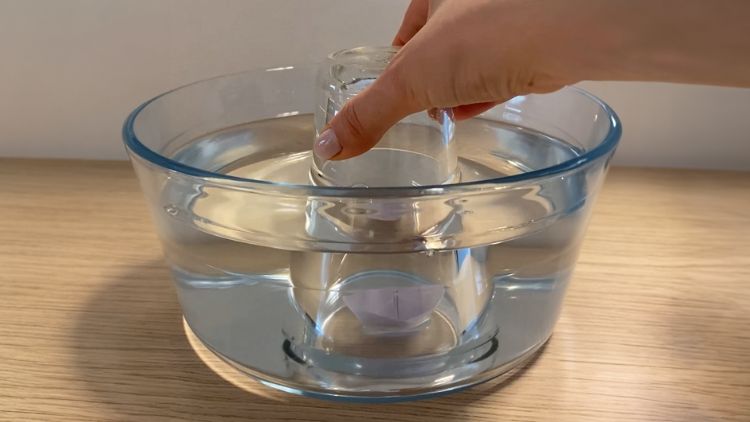 Ein Experiment bei dem mit einer Schüssel Wasser und einem Stück Papier gezeigt wird, dass ein leeres Glas voller Luft ist.