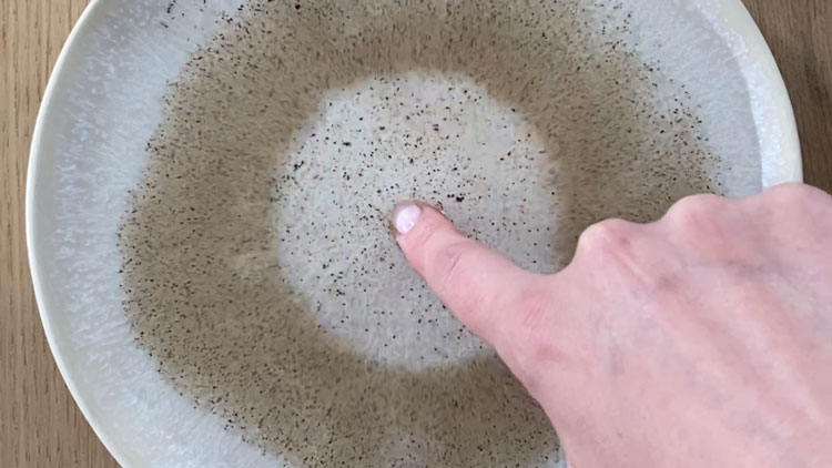 Kind berührt mit dem Finger eine mit Pfeffer bestreute Wasseroberfläche