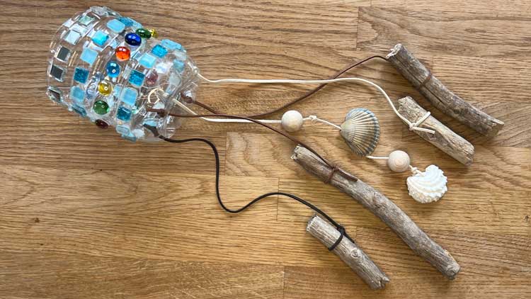 Mit einer Plastikflasche und ein paar Schnüren und Mosaiksteinen wird ganz schnell ein sommerliches Windspiel gebastelt.