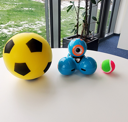 Dash-Roboter steht zwischen einem Fußball und einem Tennisball