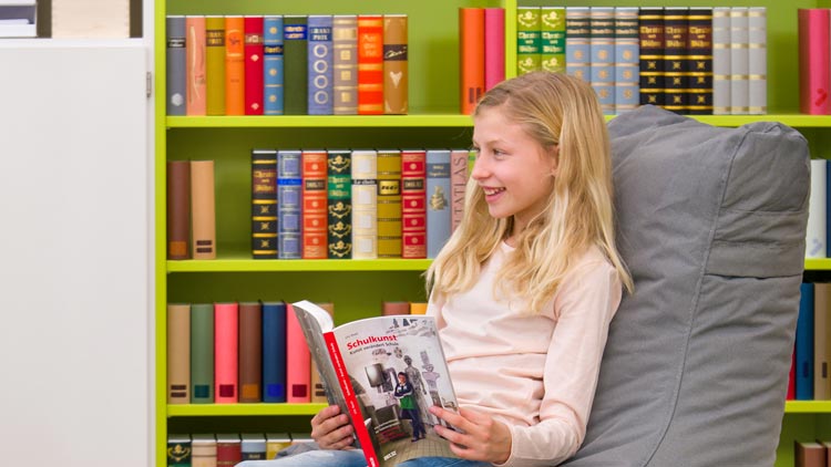 Mädchen vor Bücherregal am Lesen