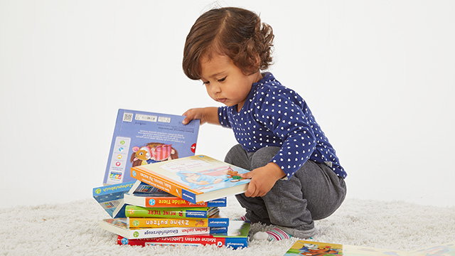 Kind sucht sich Buch aus einem Stapel von Büchern aus