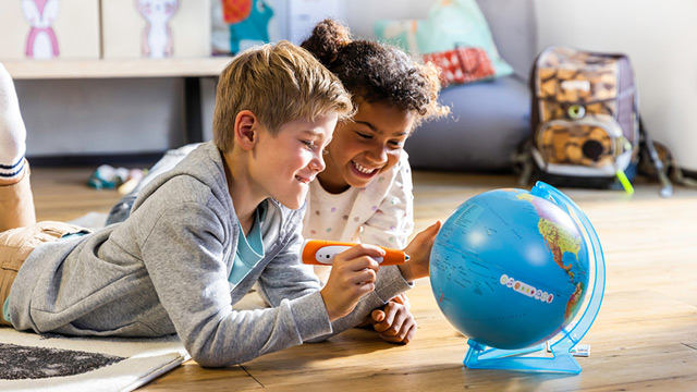 Kinder liegen auf dem Boden und nutzen den tiptoi Stift, um die Welt auf einem Globus zu entdecken